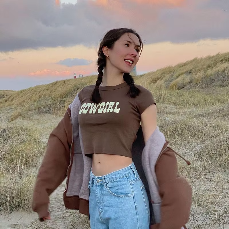 Brown cowgirl crop top with bold white lettering, short sleeves, and a trendy relaxed fit. Western-inspired casual fashion.
